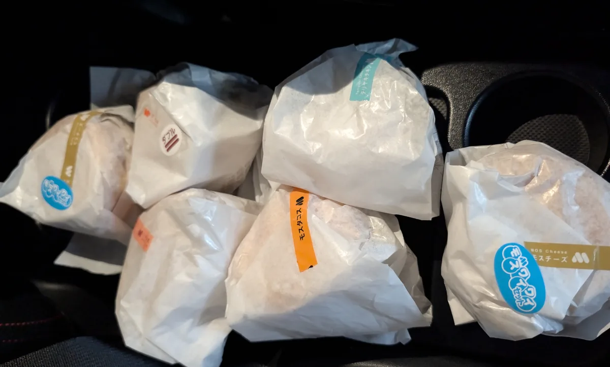 車内に並べた家族分のバーガー。テリヤキチキンバーガー、タコスバーガー、ワイワイモスのチーズバーガー2つ、ダブルチーズバーガー、海老カツバーガーを購入しました。