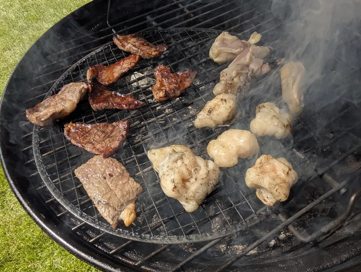 数種類のお肉をBBQコンロいっぱいに並べて焼く様子